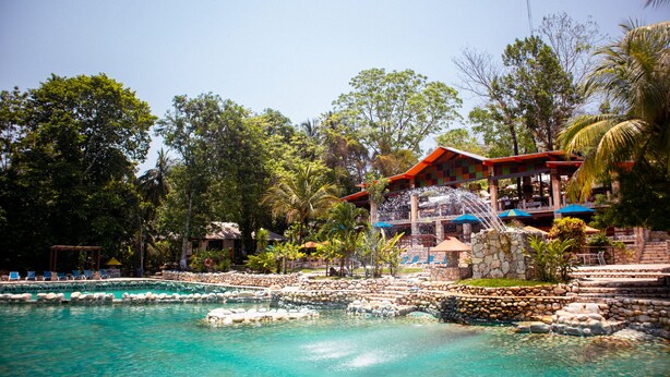 Un resort con zona de piscina, estructuras de piedra y un edificio con techo rojo.
