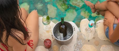 Two people sitting by a pool with a bucket containing a bottle and glasses.