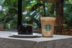 Un postre y un café helado Starbucks sobre una mesa con vistas a zonas verdes.