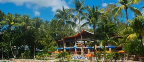 Un resort con piscina, palmeras y un edificio con varios balcones.