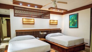 Habitación de hotel con dos camas de madera, un ventilador de techo y una lámpara fijada a la pared.