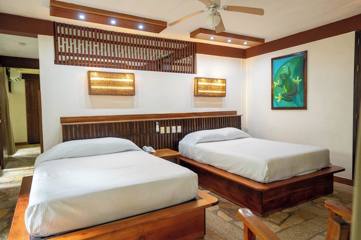 Ein Hotelzimmer mit zwei Holzbetten, einem Deckenventilator und einer wandmontierten Lampe.