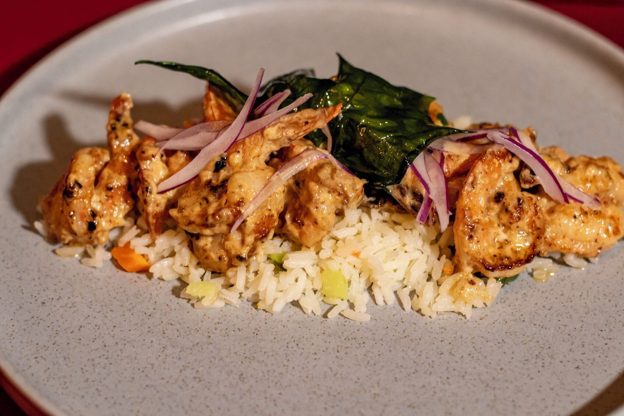 A plate of food with rice and chicken, garnished with red onion and greens.