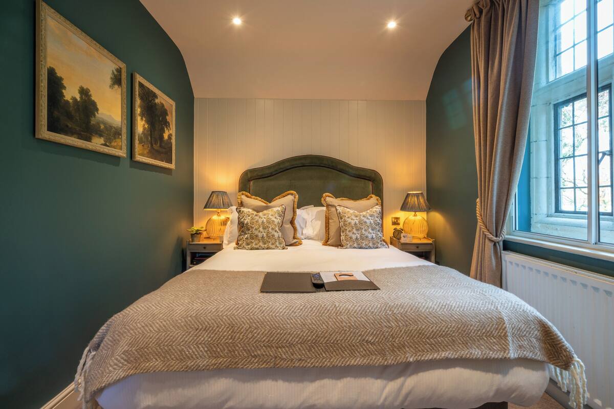 A neatly made bed with a headboard, two bedside lamps, and two framed landscape paintings on the wall.