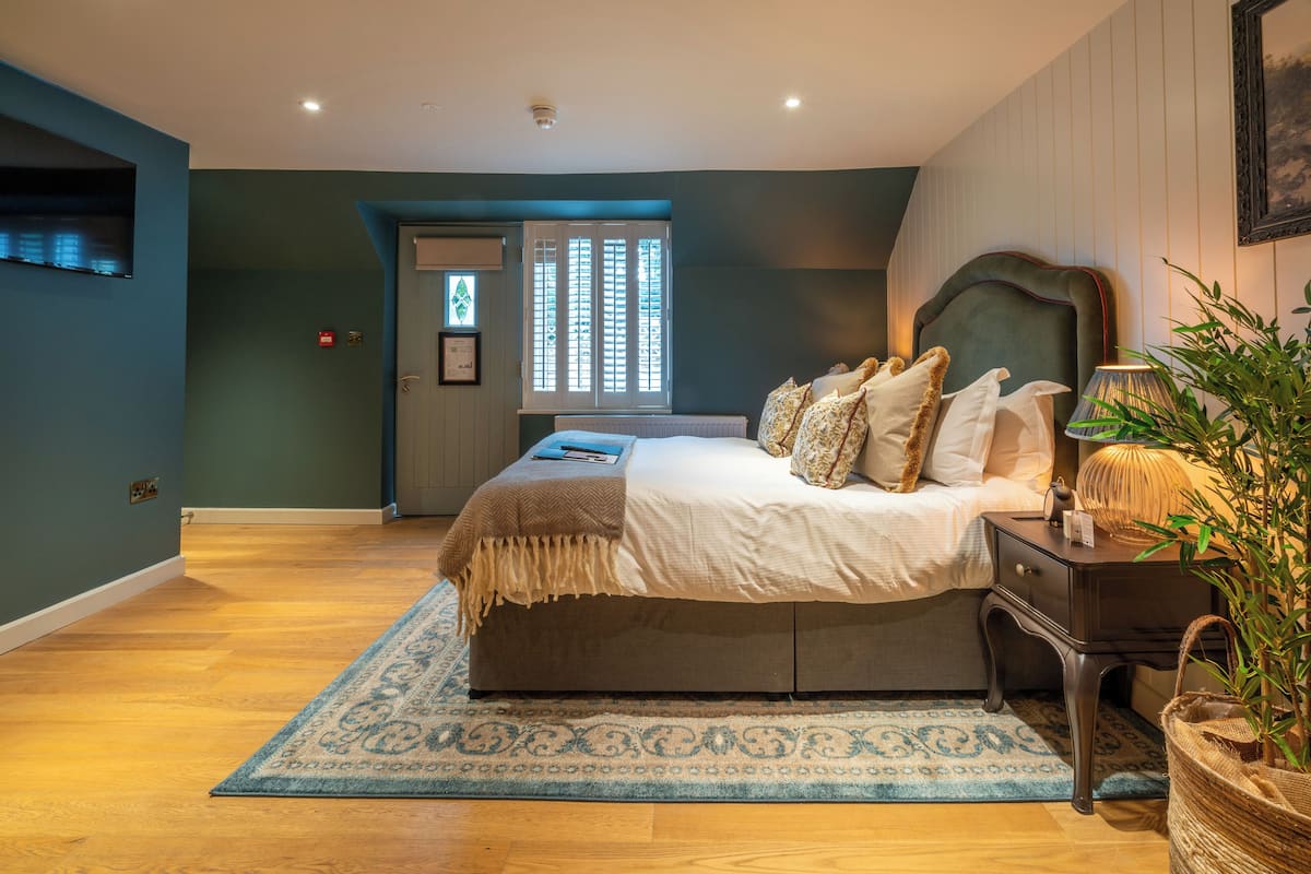 A bedroom with a bed, bedside table, lamp, and a window with blinds.