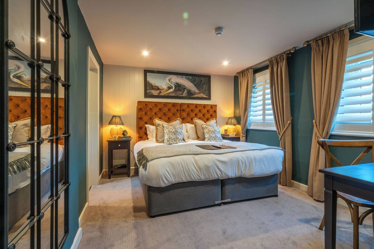 A bedroom with a large bed, a nightstand, a desk, and a chair.