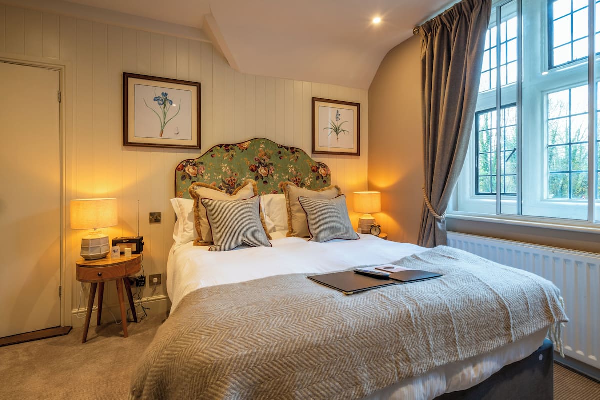 A neatly arranged bedroom with a bed, bedside tables, lamps, and framed botanical prints on the wall.