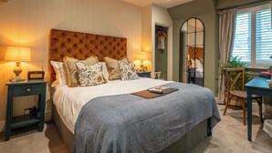 A bedroom with a large bed, bedside tables, a desk, and a mirror. - The Northey Arms (Corsham)