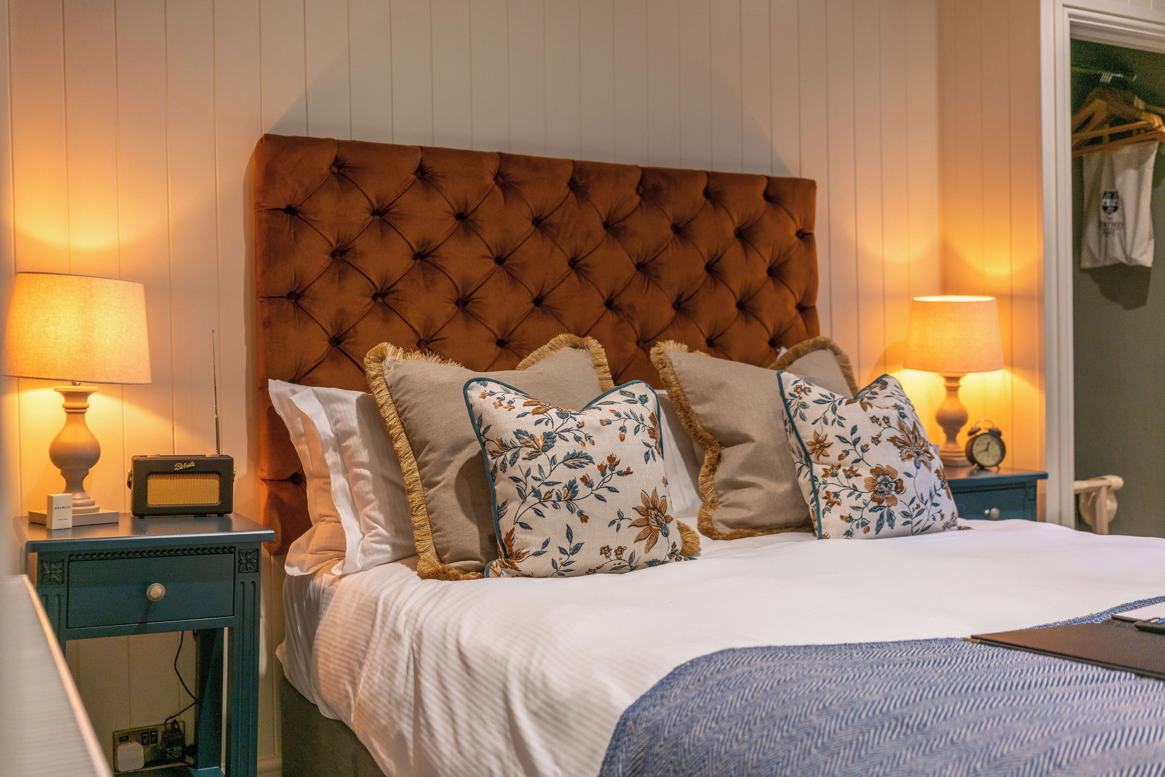 A neatly made bed with a tufted headboard, flanked by two bedside tables with lamps and a radio.