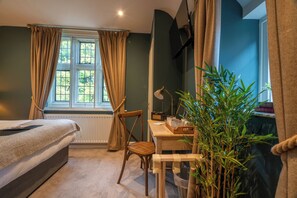 Quarto com cama, cadeira, escrivaninha, planta em vaso e janela com cortinas.