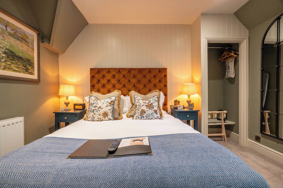 A hotel room with a large bed, two bedside tables with lamps, a wooden headboard, and a wardrobe.