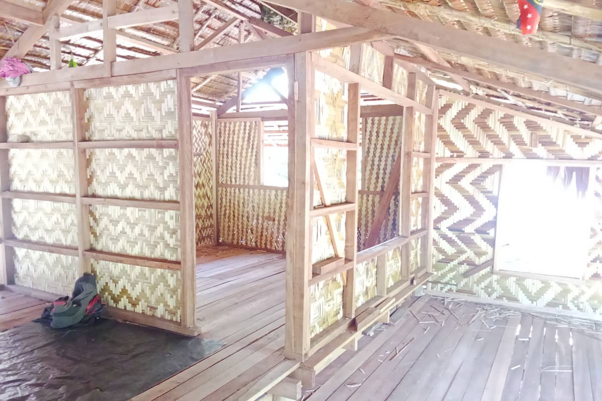 A wooden structure with a thatched roof, featuring a patterned wall and a bench area.