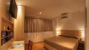 Habitación de hotel con cama, escritorio, silla, televisor y ventana con cortinas.