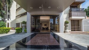 Entrada de un edificio moderno con puerta de vidrio, piso de mármol y un pequeño jardín con plantas en macetas.