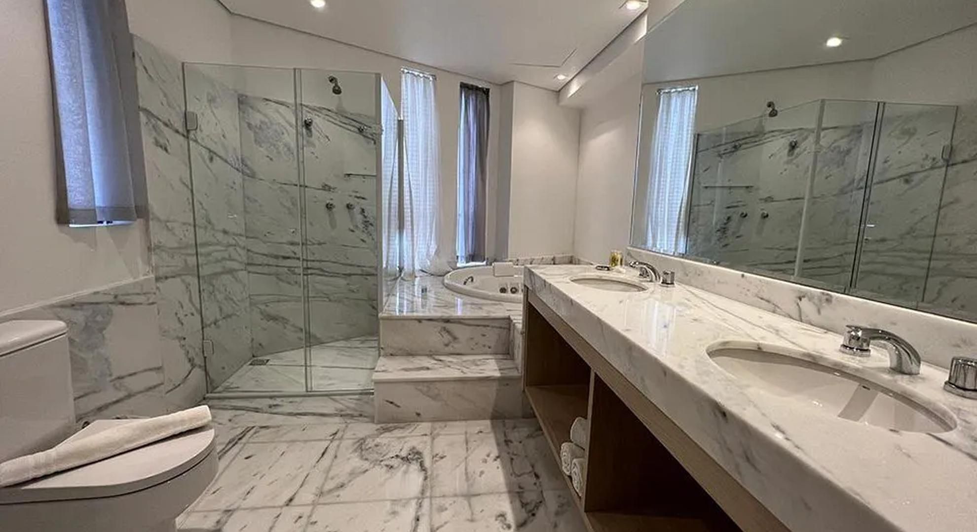 Um banheiro moderno com piso de mármore, um espelho grande, uma banheira e uma pia dupla.