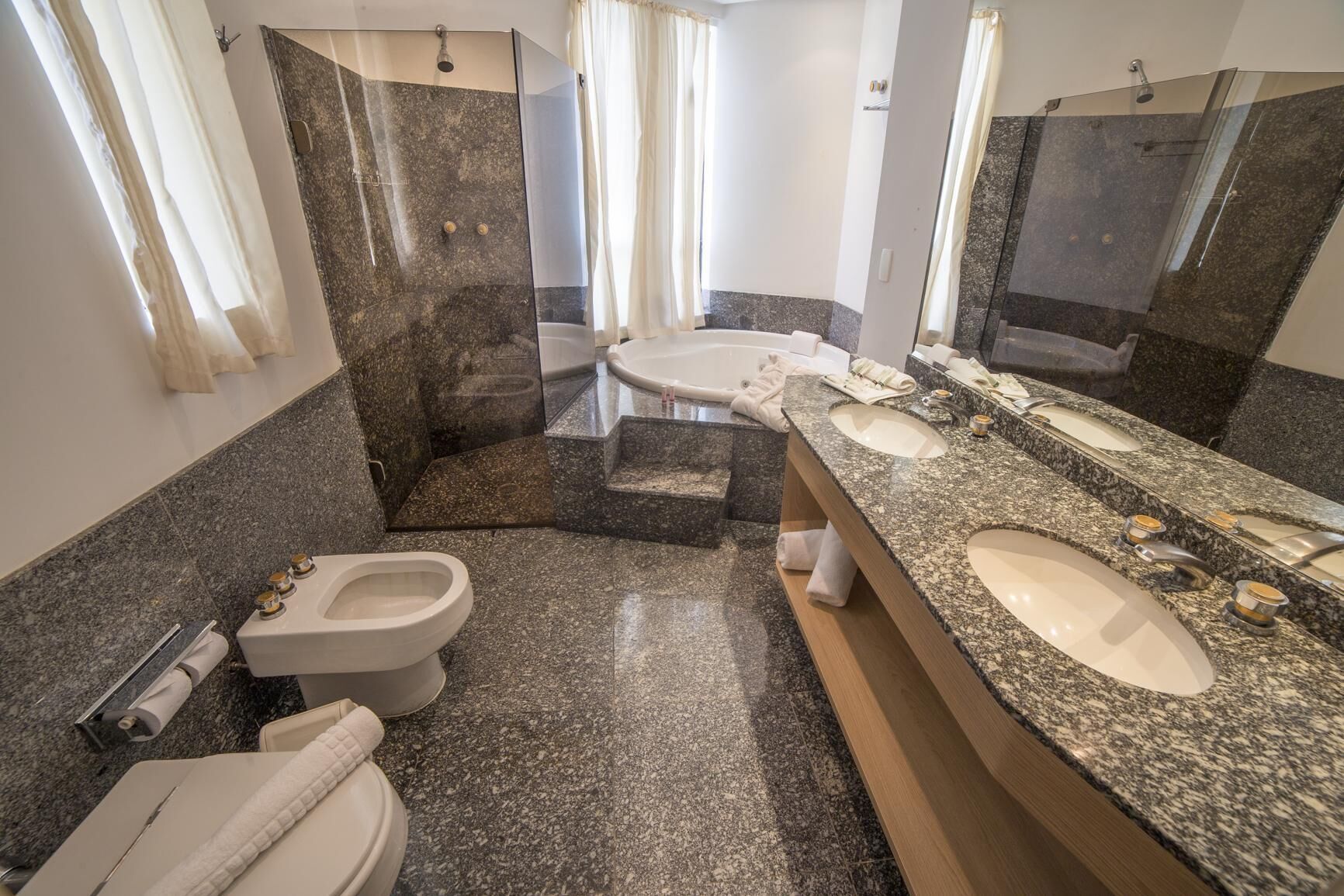 A modern bathroom with a granite countertop, two sinks, a shower, and a toilet.