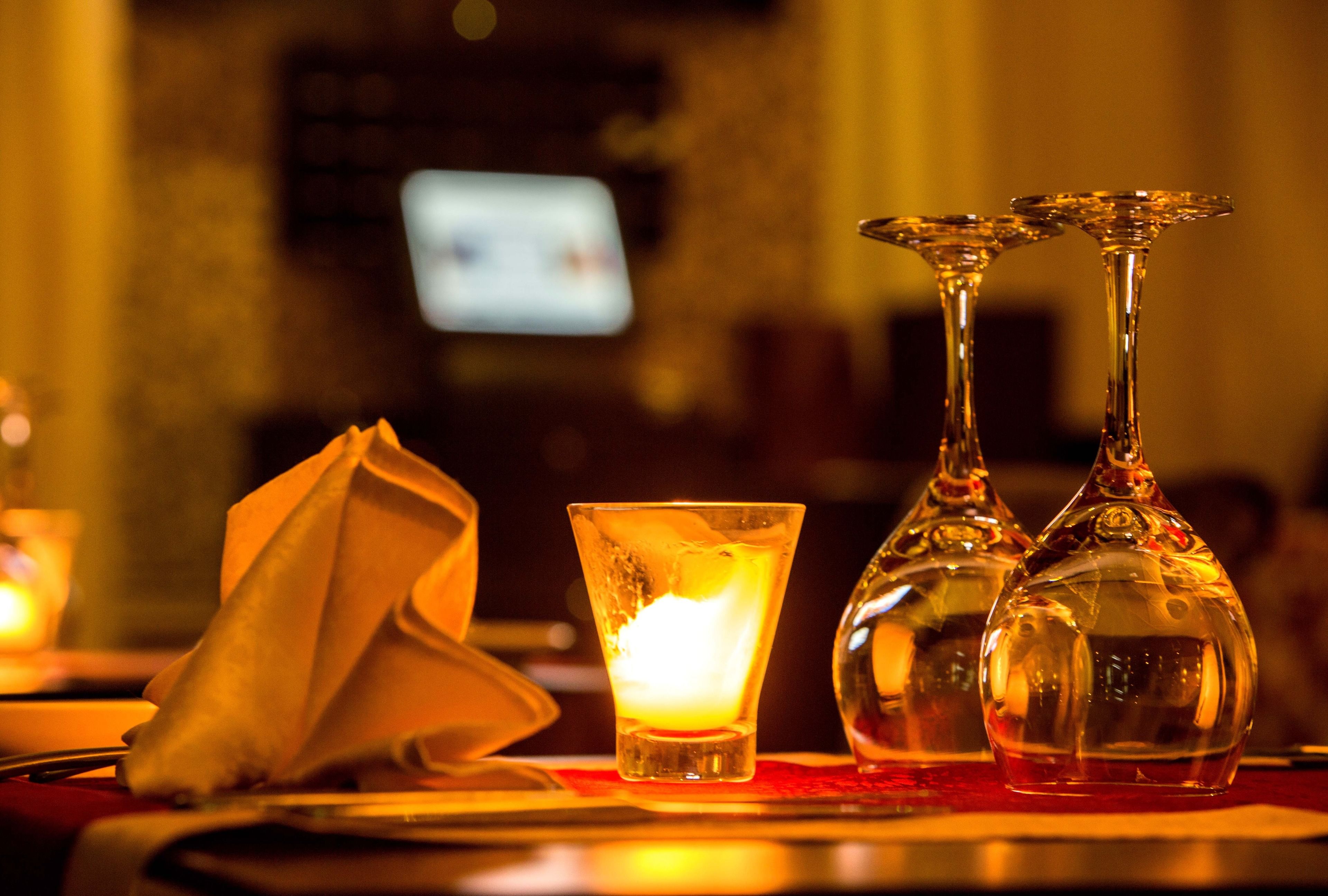 A bar setting with a candle, a napkin, and two glasses on a table.