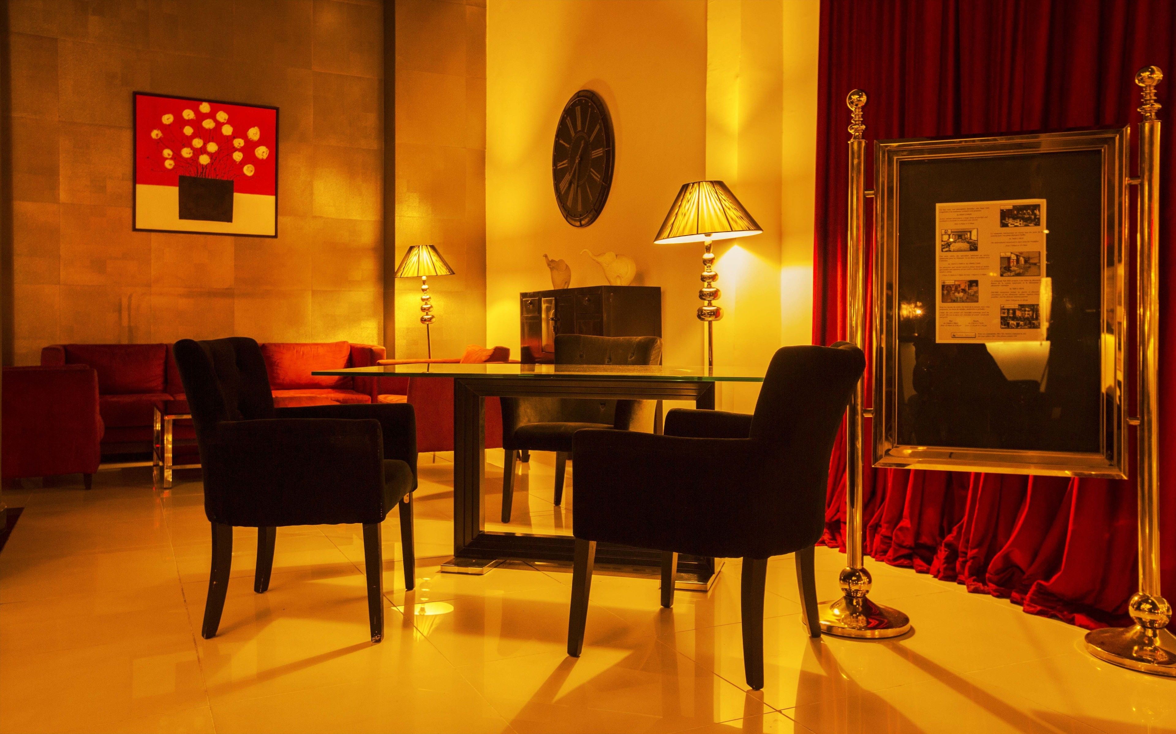 A hotel room with a red sofa, two armchairs, a glass table, and a red curtain.