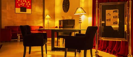A hotel room with a red sofa, two armchairs, a glass table, and a red curtain.