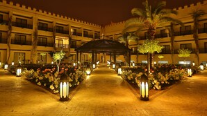 A hotel courtyard at night with a central gazebo, palm trees, and flower beds. - Adam Park Hotel & Spa Marrakech (Marrakech)