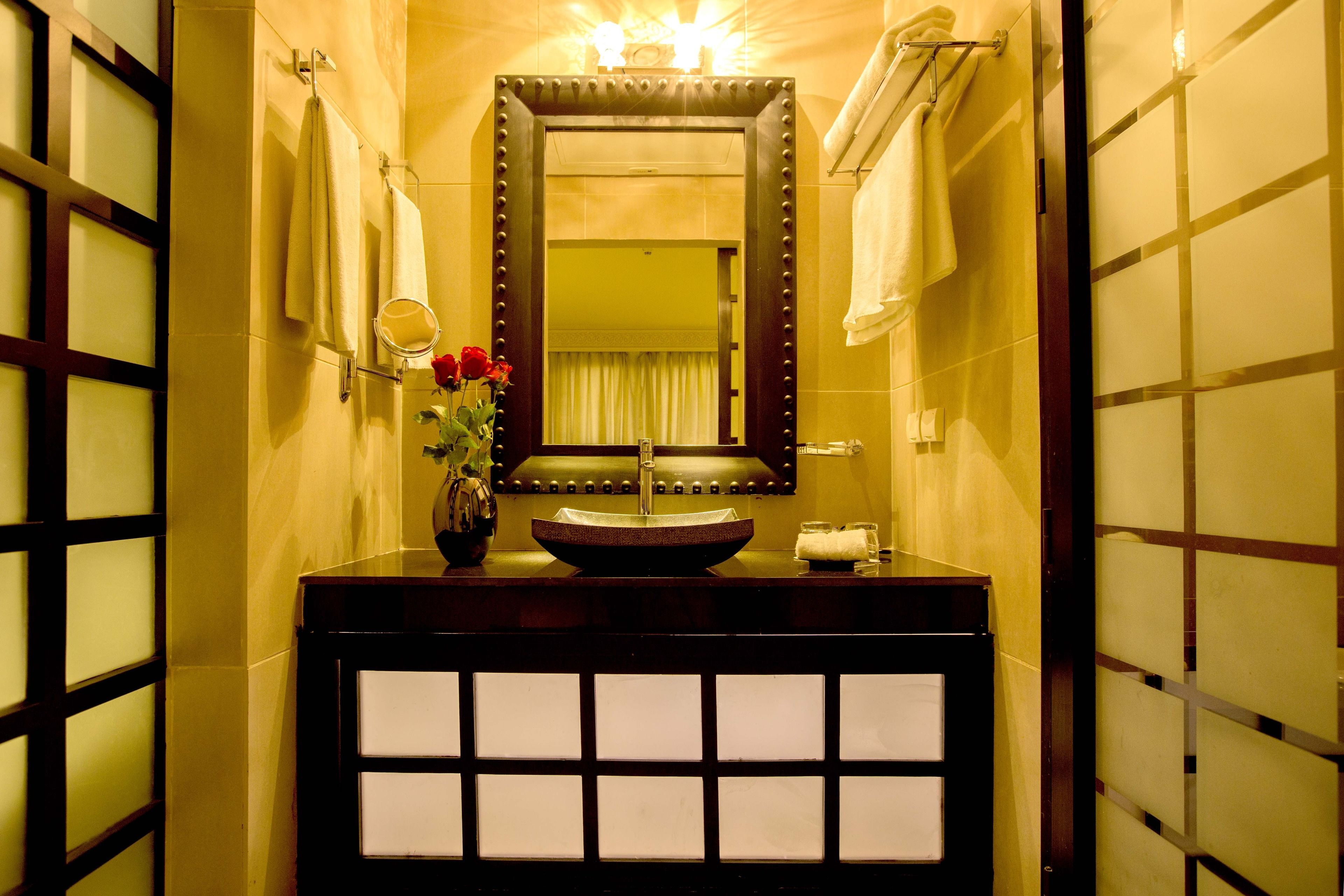 A bathroom with a large mirror, a sink, and a vase with flowers.
