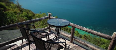 A wooden deck with a glass table and two chairs overlooking a coastal view.