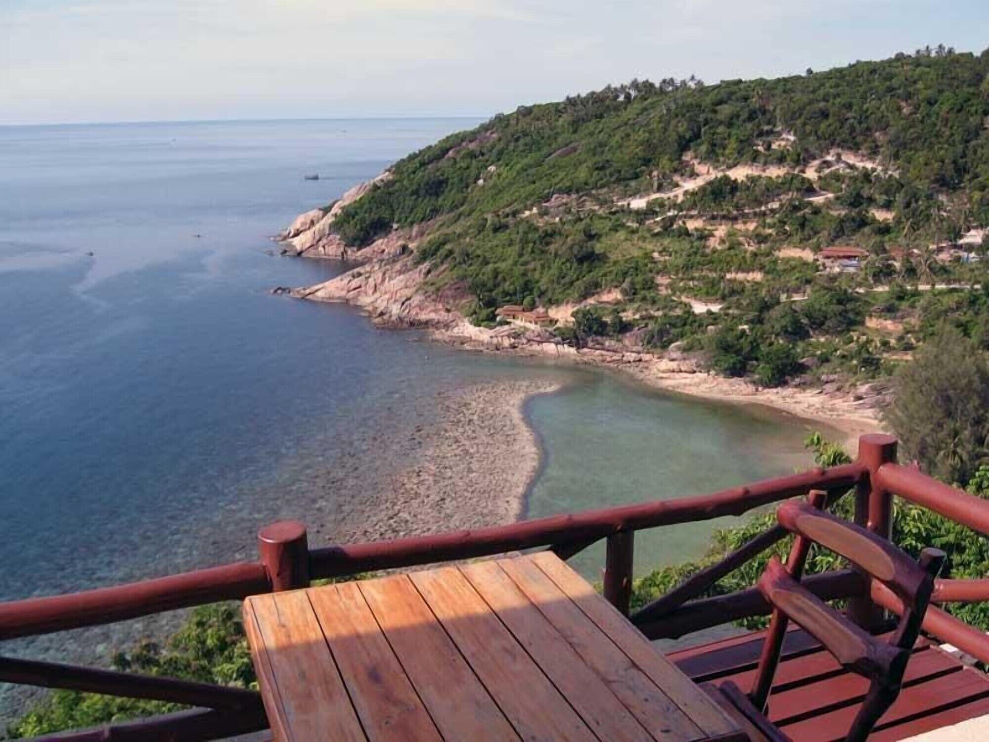 Une terrasse en bois offrant une vue sur un paysage côtier, comprenant une plage et une colline couverte de végétation.