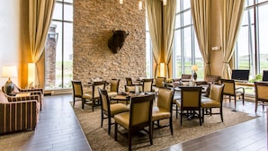 A hotel lobby with a stone wall, leather chairs, tables, and large windows.
