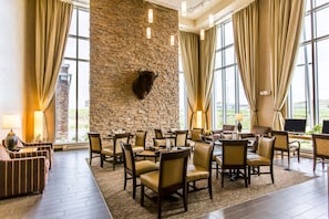 Un hall d’hôtel avec un mur en pierre, des fauteuils en cuir, des tables et de grandes fenêtres.