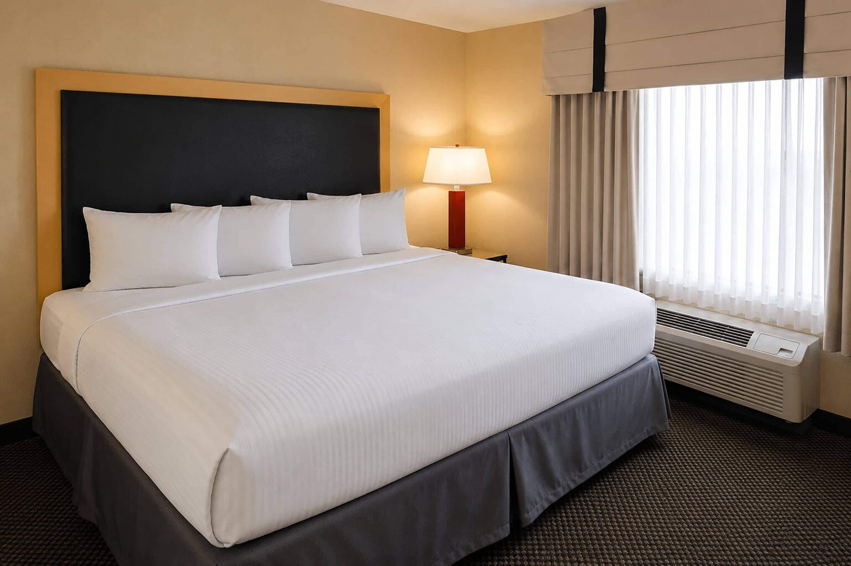 Hotelkamer met een groot bed, een bedlamp, een raam met gordijnen en een wandairconditioner.