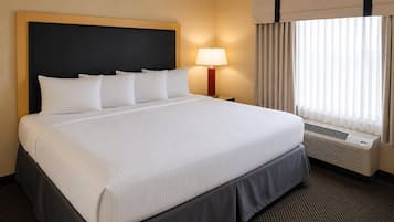 Hotelkamer met een groot bed, een bedlamp, een raam met gordijnen en een wandairconditioner.