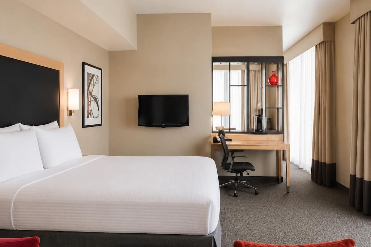Une chambre d’hôtel avec un lit, un bureau, une chaise, une télévision et une fenêtre avec des rideaux.