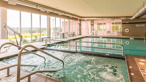 An indoor swimming pool with clear glass walls, a lifeguard station, and a poolside area with chairs and tables.