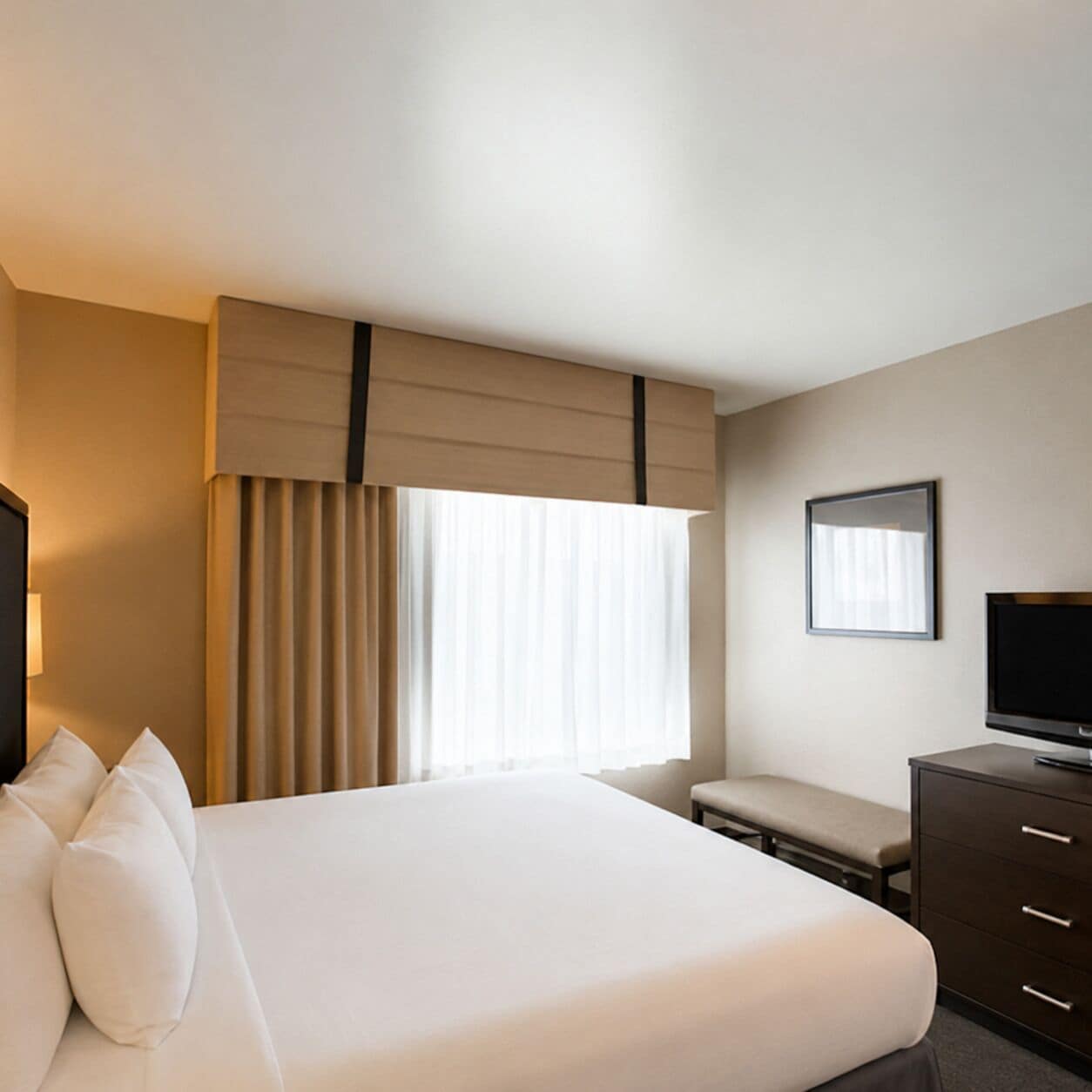 Habitación de hotel con cama, televisión, escritorio y ventana con cortinas.