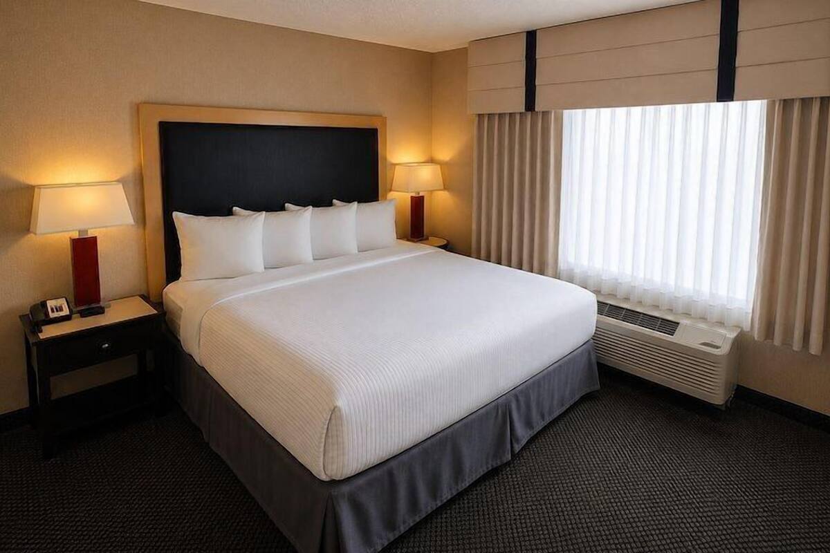 Une chambre d’hôtel avec un grand lit, des lampes de chevet, une fenêtre avec des rideaux et un climatiseur fixé au mur.
