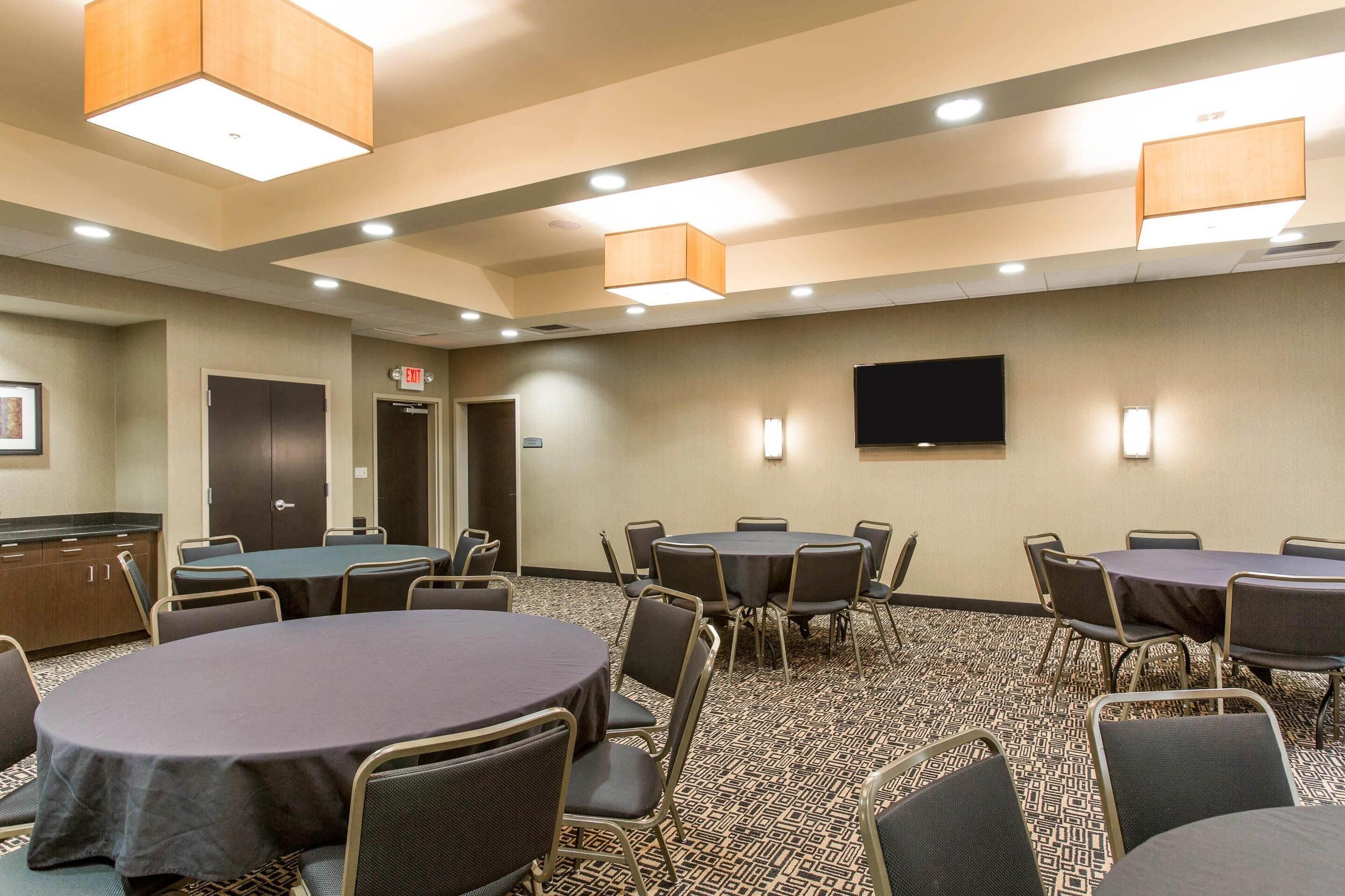Une salle de conférence équipée de plusieurs tables et chaises, d’un téléviseur à écran plat fixé au mur et d’un panneau indiquant la sortie.