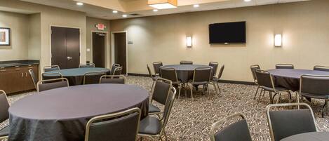 Une salle de conférence équipée de plusieurs tables et chaises, d’un téléviseur à écran plat fixé au mur et d’un panneau indiquant la sortie.