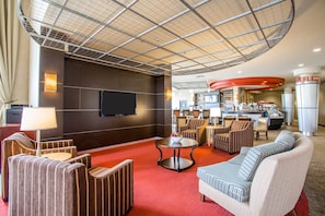 A hotel lobby with a red carpet, seating area, a television, and a kitchenette. - Cambria Hotel Rapid City near Mount Rushmore (Rapid City)