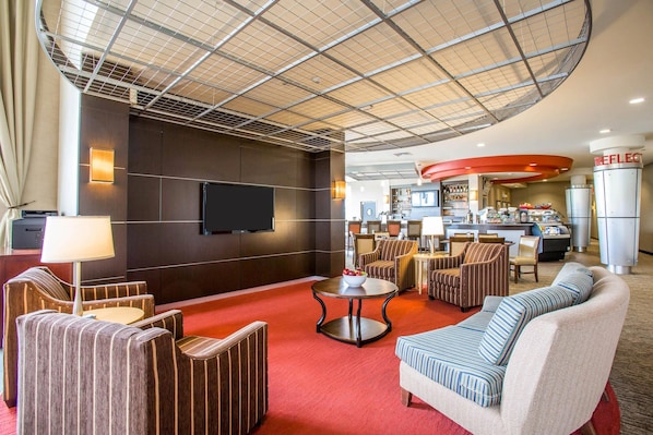 A hotel lobby with a red carpet, seating area, a television, and a kitchenette.