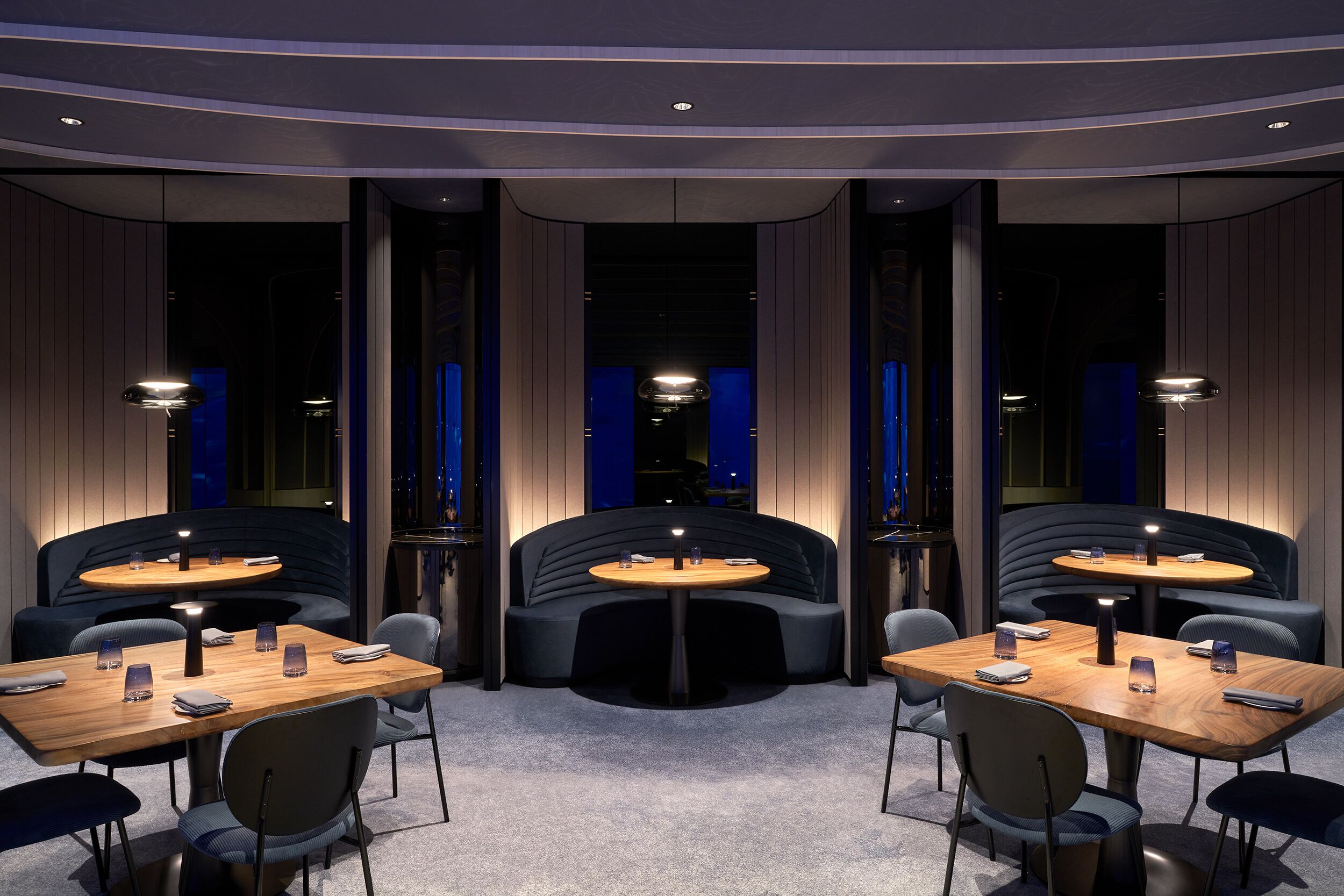 A modern hotel lobby with round tables, comfortable seating, and a central light feature.