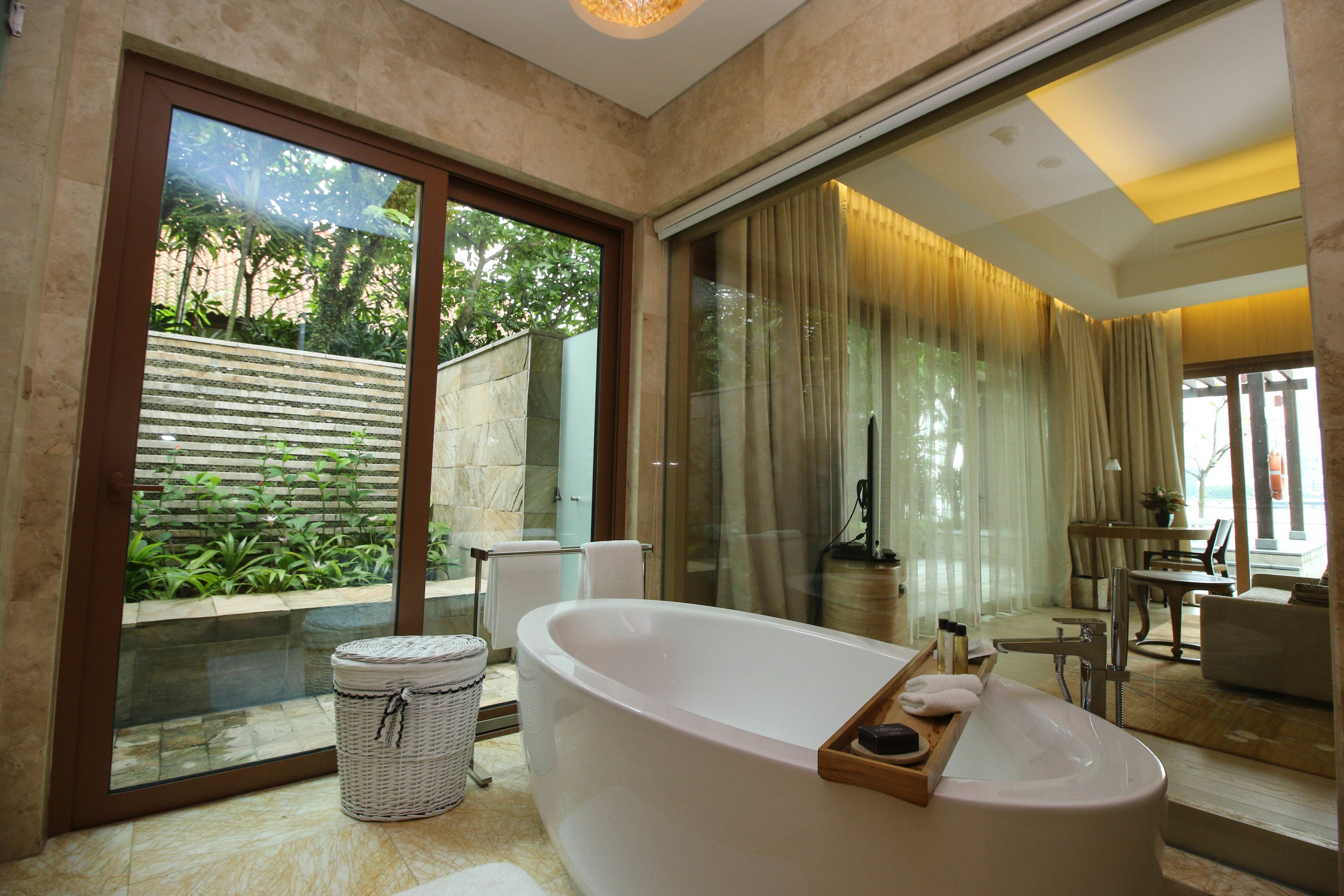 Ein modernes Badezimmer mit freistehender Badewanne, einer Glasdusche und Blick auf einen üppigen Garten.
