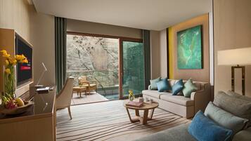 Habitación de hotel moderna con sofá, una mesa de centro, televisor y balcón con pared de piedra.