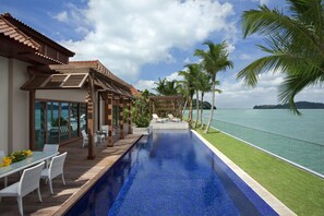 Un área junto a la piscina con vista despejada al mar, un espacio de descanso cubierto y una zona de comedor.