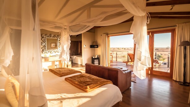 A bedroom with a large bed, a sitting area, and a view of the desert. - Bagatelle Kalahari Game Ranch (Mariental)