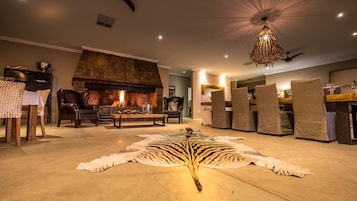 Una sala de estar con chimenea, sillones de cuero, una mesa de comedor con copas de vino y un tapete grande de piel de animal.