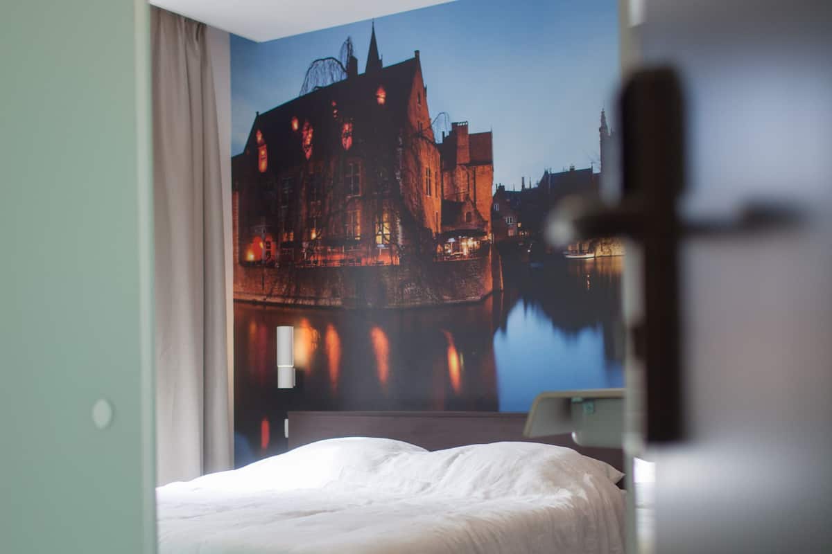 Habitación de hotel con cama, mesita de noche y un mural en la pared que representa un castillo junto a un lago.