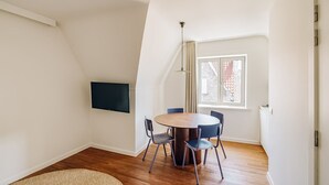 Un comedor moderno con una mesa redonda, cuatro sillas, un televisor de pantalla plana en la pared y una ventana con vista a un edificio.