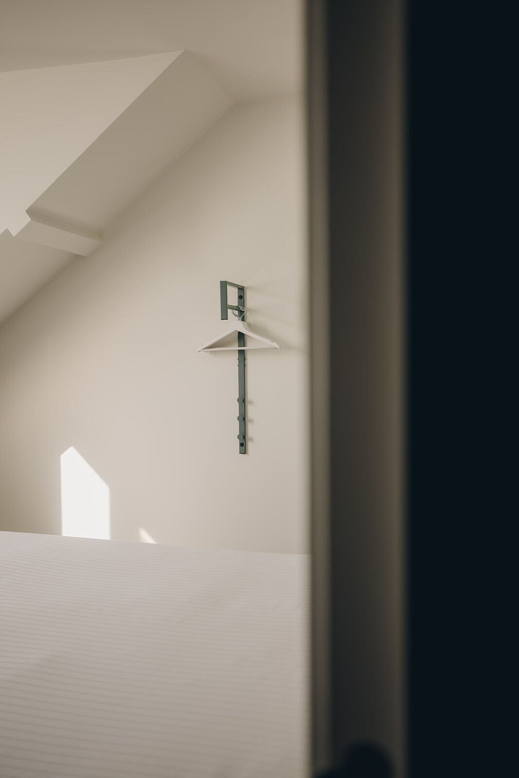 Une pièce avec un plafond en pente, un luminaire suspendu et une fenêtre qui projette une ombre.