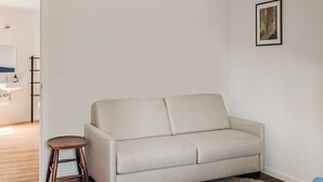 Una sala de estar minimalista con un sofá, un taburete pequeño y una mesa de comedor con sillas.