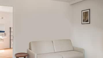 Una sala de estar minimalista con un sofá, un taburete pequeño y una mesa de comedor con sillas.